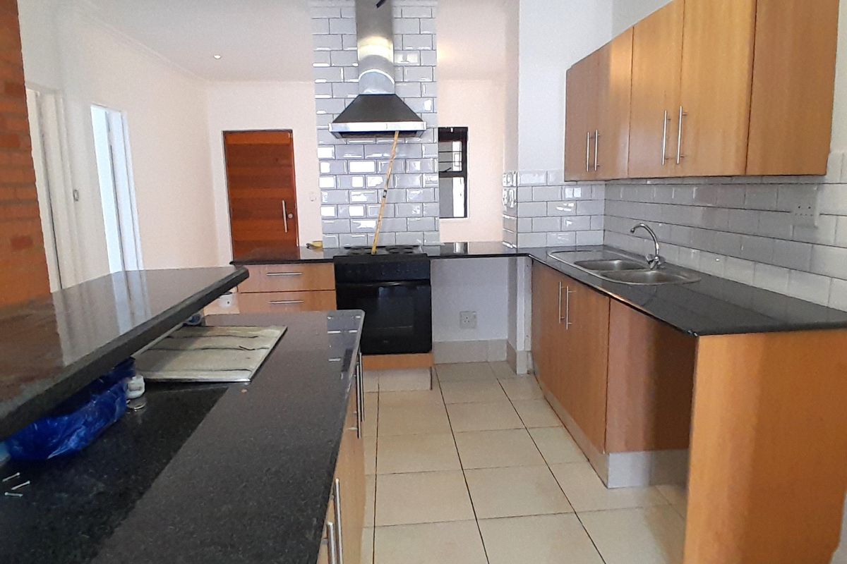 A functional kitchen featuring wooden cabinetry, granite countertops, a subway tile backsplash, and a built-in oven with a stainless steel extractor fan.