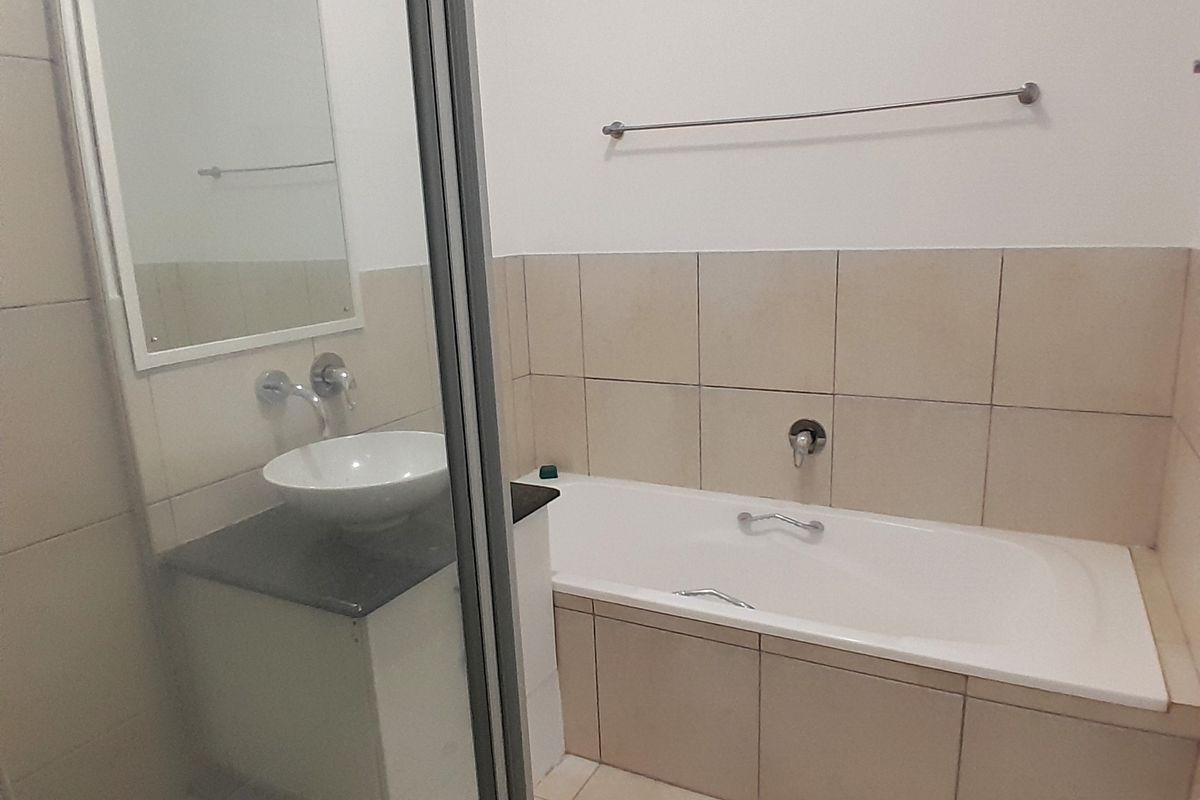 A clean, functional bathroom featuring a built-in bathtub, a modern vessel sink on a vanity cabinet, and a separate glass-enclosed shower area.