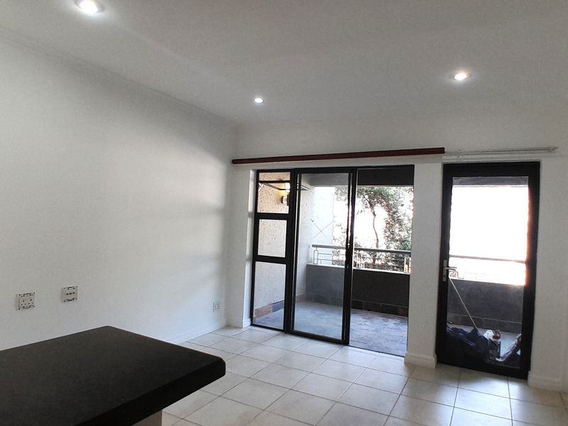 An open-plan living area featuring tiled flooring, recessed lighting, and direct access to a private balcony through sliding glass doors.