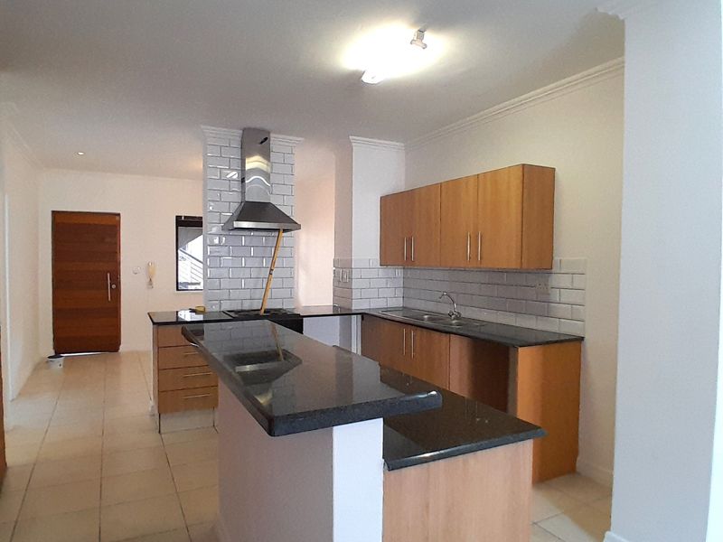 A clean, functional kitchen featuring wooden cabinetry, dark granite countertops, a subway tile backsplash, and a stainless steel extractor fan.
