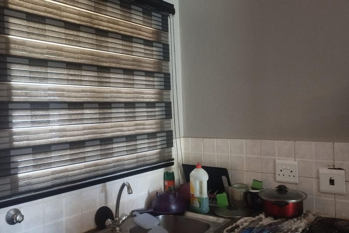 A kitchen corner featuring a stainless steel sink, mixer tap, tiled splashback, and a modern roller blind over the window.