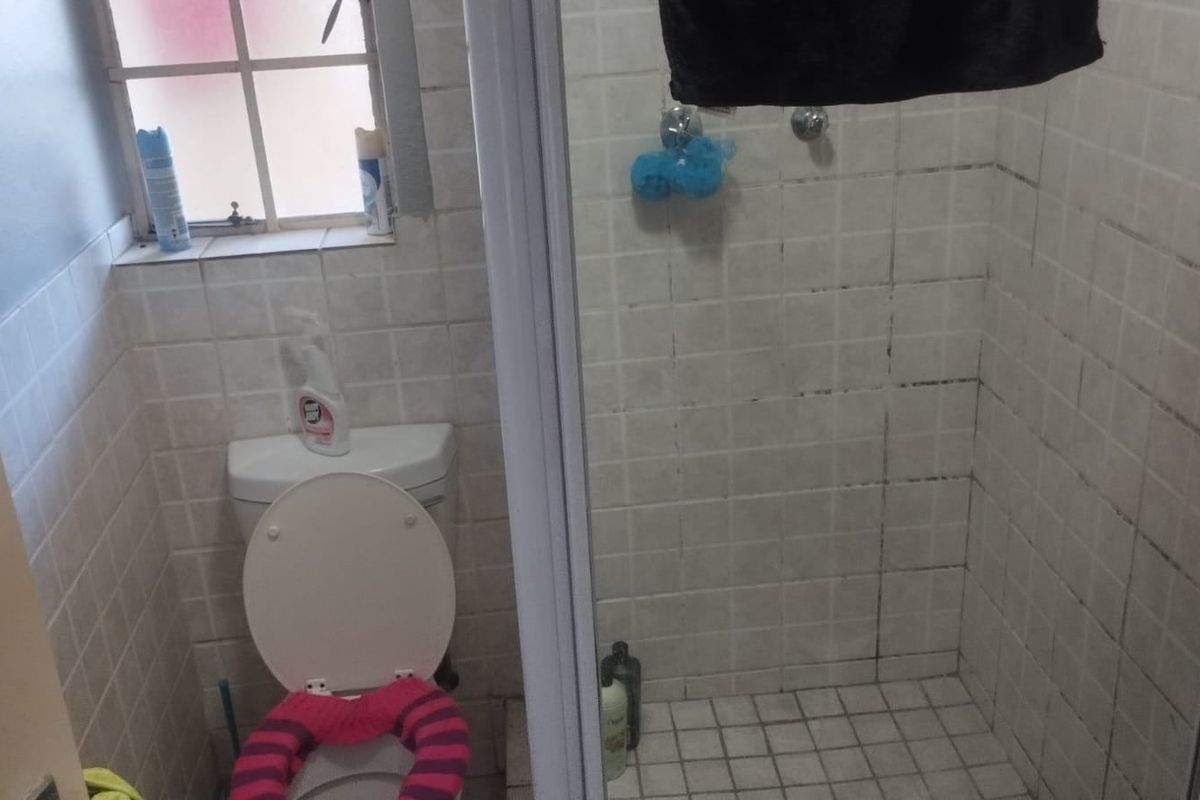 A compact bathroom featuring a shower enclosure and toilet, with tiled finishes throughout requiring maintenance and cleaning.