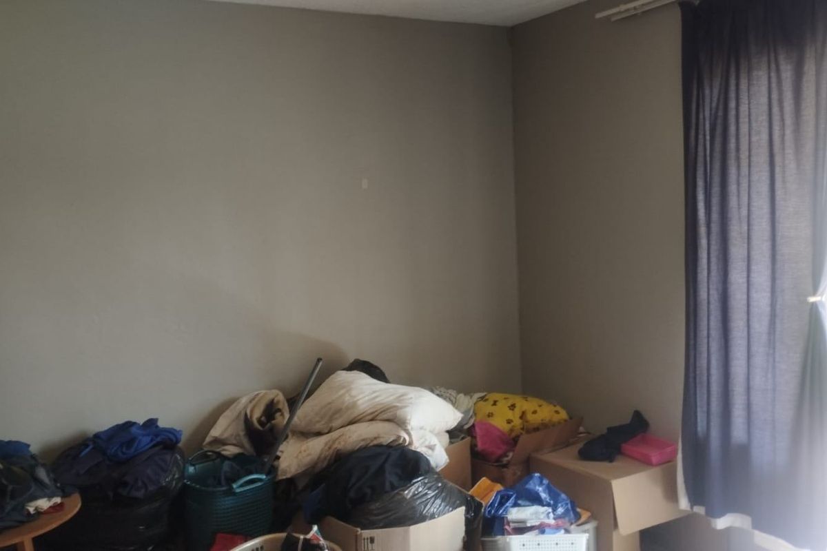 A bedroom space featuring neutral wall finishes and a curtain rail, currently used for storage.