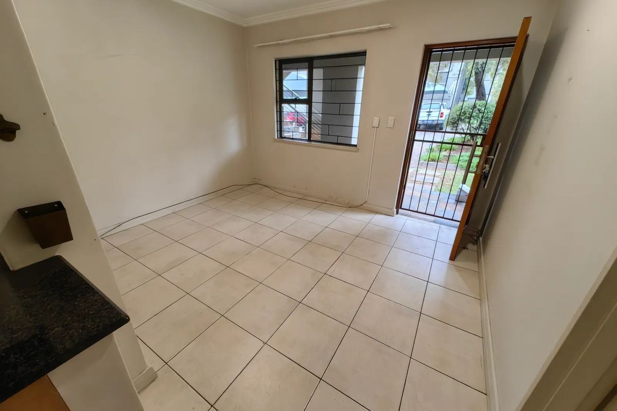 An empty living area featuring tiled flooring, a security gate, and a window with security bars, offering a blank canvas for potential updates.