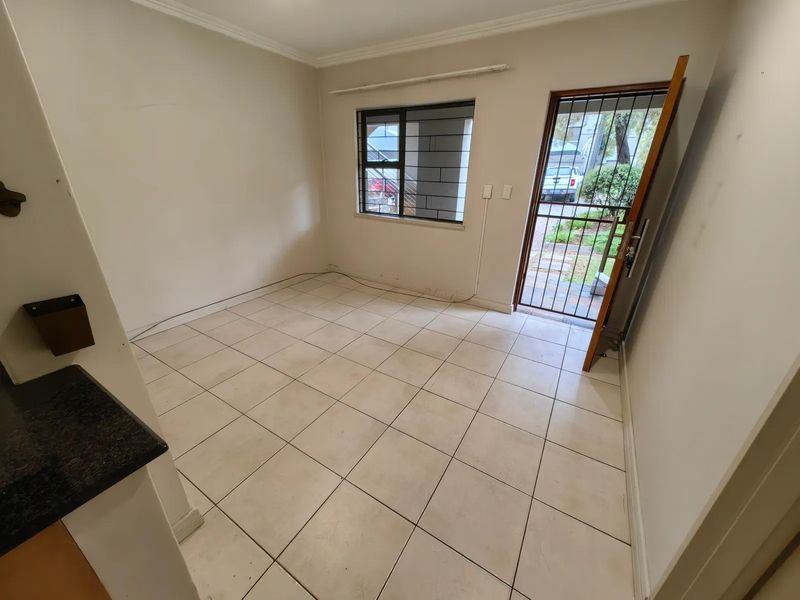 An empty living area featuring tiled flooring, a security gate, and a window with security bars, offering a blank canvas for potential updates.