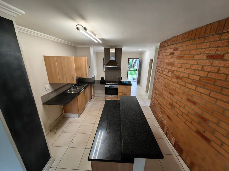 Spacious kitchen featuring granite countertops, built-in oven with gas hob, stainless steel extractor, and a central island, complemented by an exposed brick feature wall.