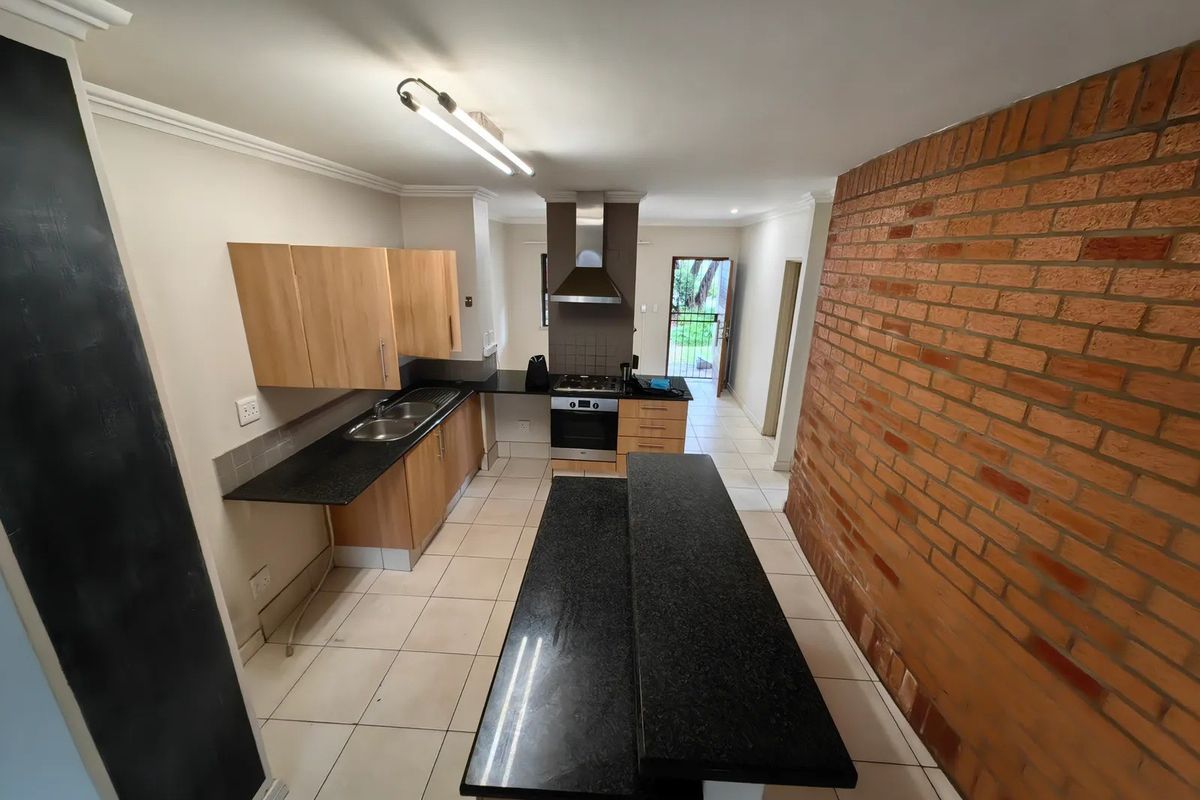 Spacious kitchen featuring granite countertops, built-in oven with gas hob, stainless steel extractor, and a central island, complemented by an exposed brick feature wall.