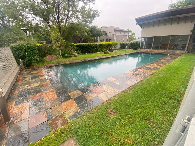 A private swimming pool area featuring a slate tile surround, lush garden landscaping, and an adjacent covered patio space.