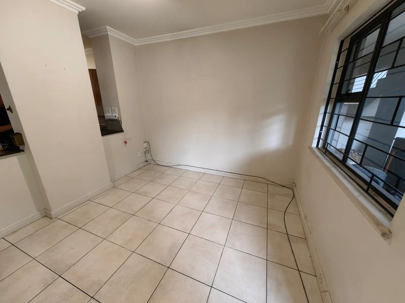An empty living area featuring ceramic floor tiles, security bars on the window, and neutral wall finishes, ready for personalization.
