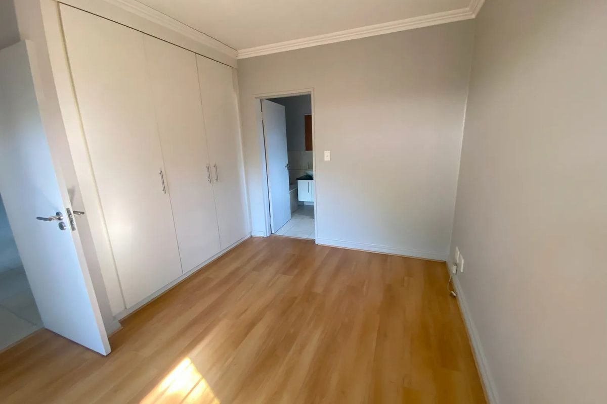 A bright, empty bedroom featuring laminate flooring, built-in cupboards, and direct access to an adjoining bathroom.
