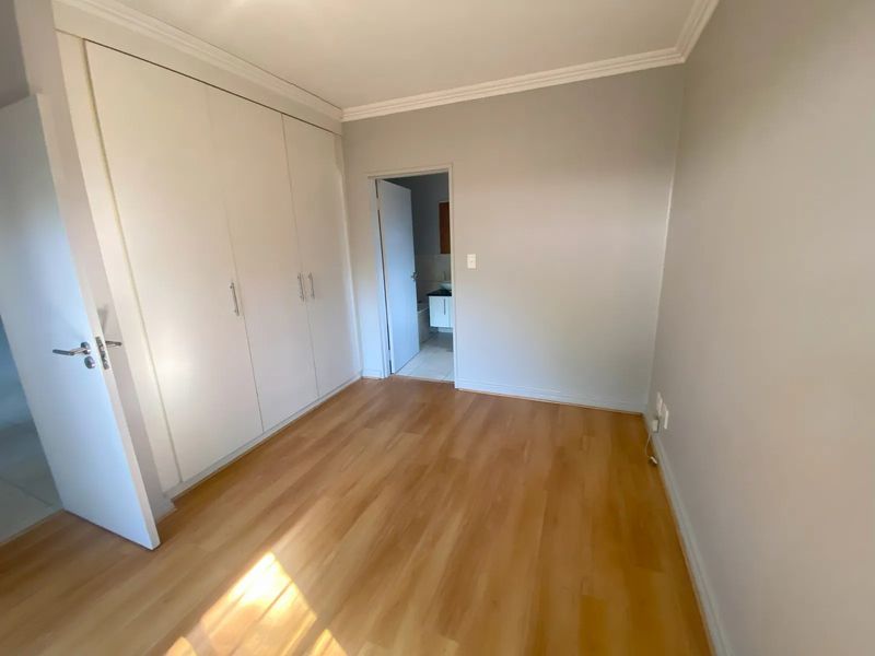 A bright, empty bedroom featuring laminate flooring, built-in cupboards, and direct access to an adjoining bathroom.