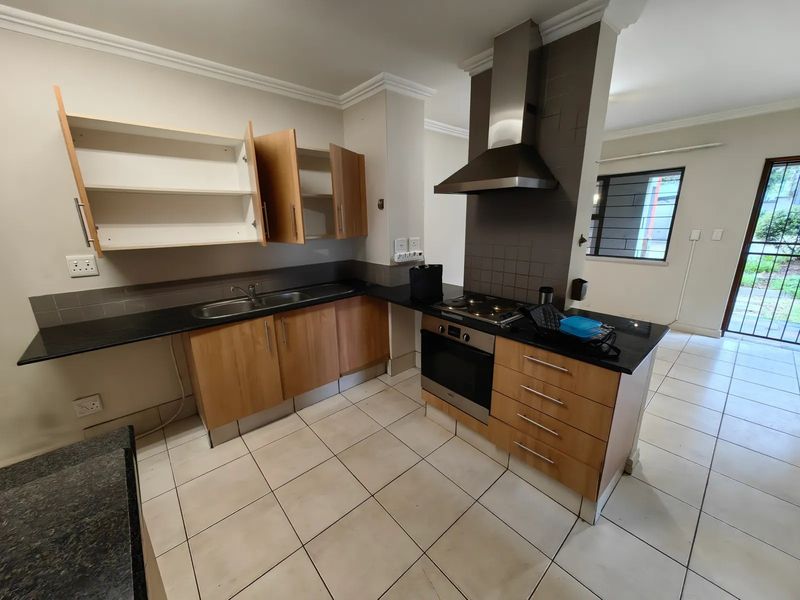 A functional kitchen featuring granite countertops, built-in oven, gas hob, and stainless steel extractor fan, with tiled flooring and ample cabinetry.