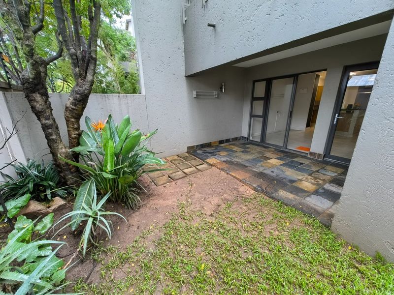 A private ground-floor patio featuring slate tiling, direct access to the interior via sliding glass doors, and an adjacent small garden area.