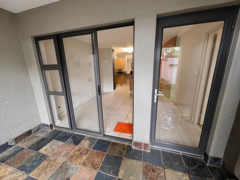 Covered patio area with slate flooring, featuring aluminium sliding and hinged doors providing access to an open-plan interior space with tiled floors.