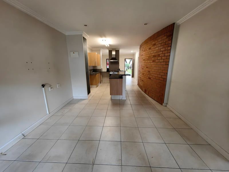 Open-plan living and kitchen area featuring tiled floors, a prominent exposed brick feature wall, and a functional kitchen layout with built-in appliances.