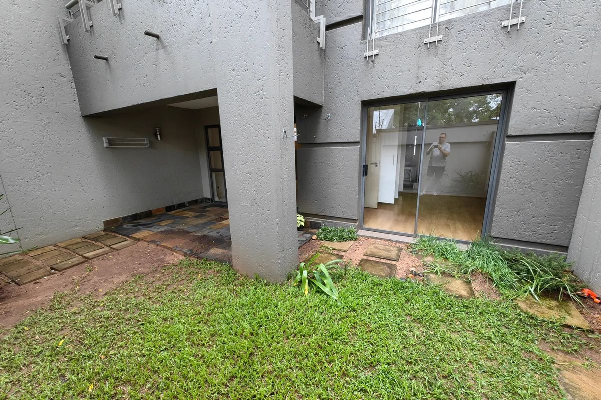 Rear exterior view of the apartment featuring a covered patio area, sliding glass doors, and a small private garden space.