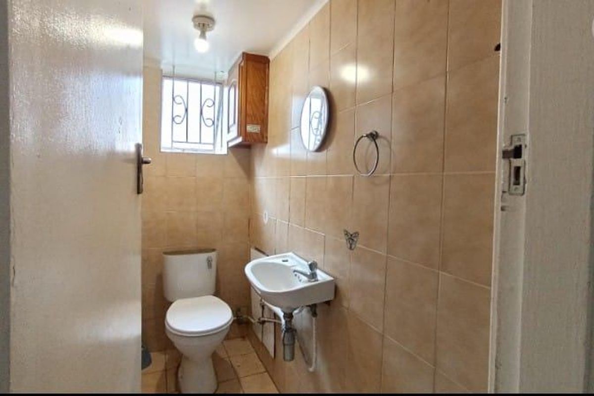 A compact bathroom featuring tiled walls and flooring, a standard toilet, and a wall-mounted basin with exposed plumbing.