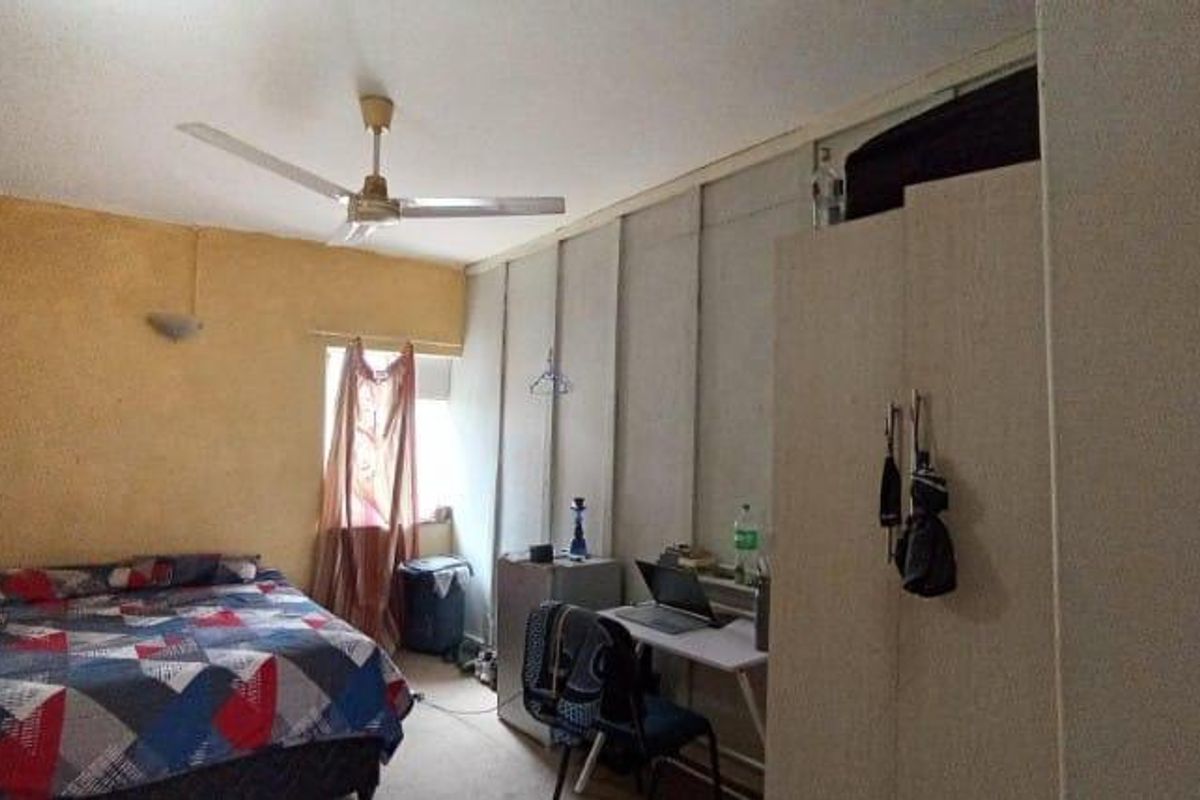 A bedroom featuring a ceiling fan, built-in wardrobe storage, and wall-mounted lighting, requiring cosmetic updates to improve the overall finish.
