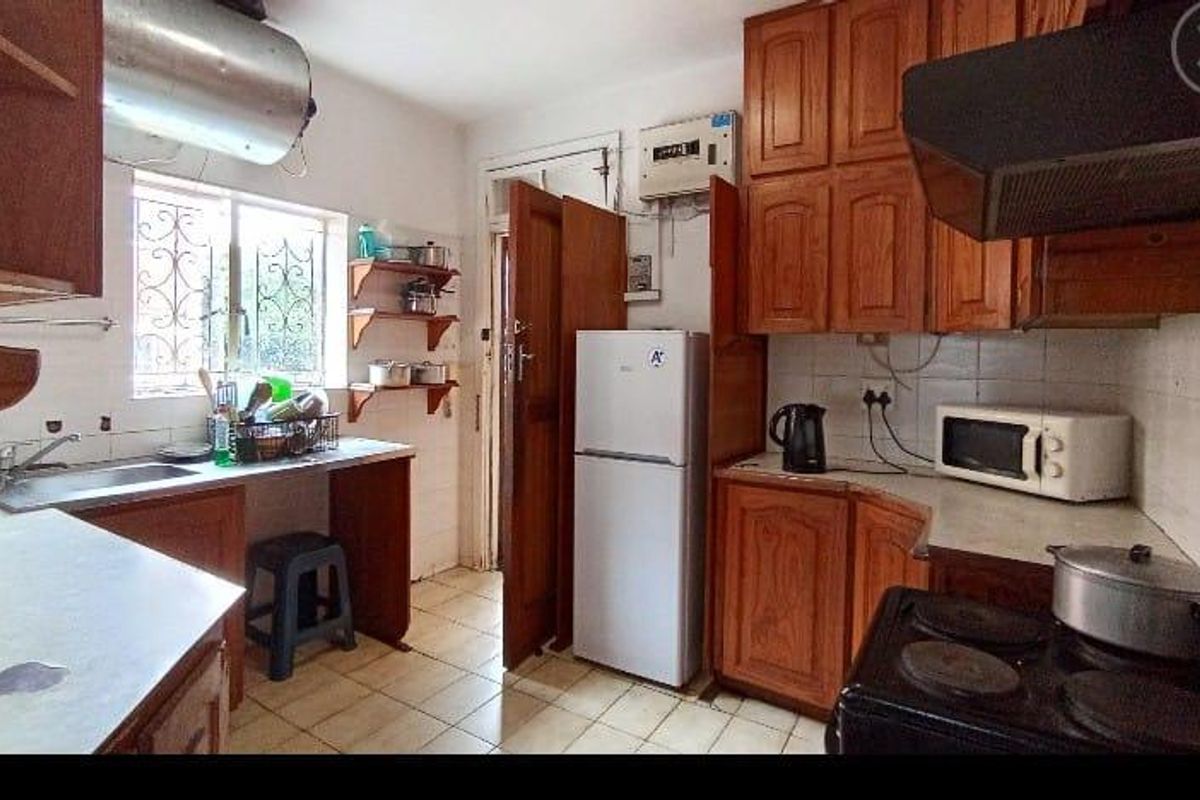 A functional kitchen featuring wooden cabinetry, tiled flooring, and a stainless steel sink, offering potential for modernization and aesthetic updates.