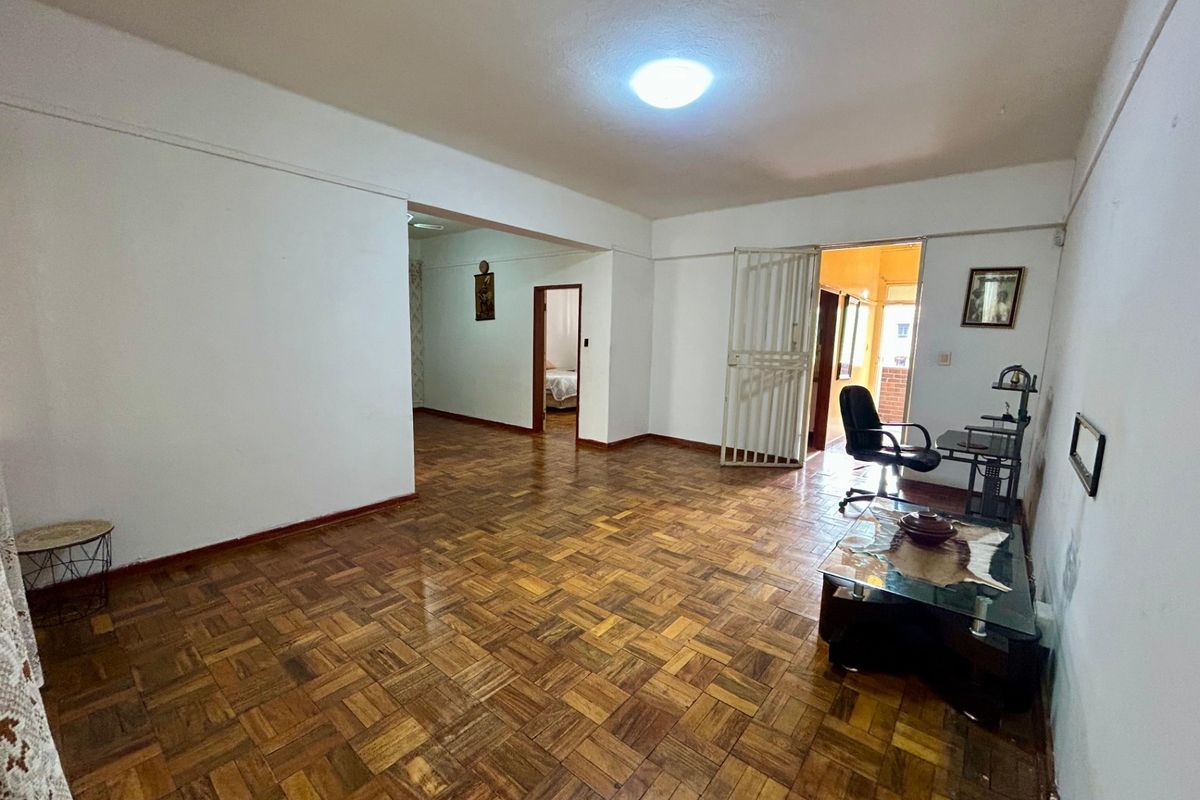 Spacious living area featuring traditional parquet flooring, neutral walls, and a security gate leading to an adjacent space.