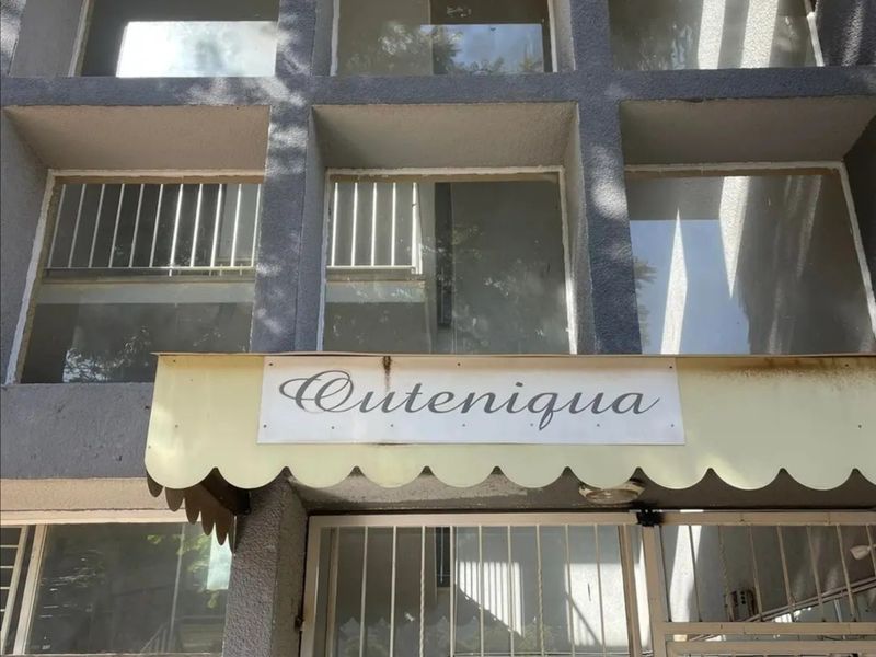Front entrance of the Outeniqua apartment building featuring a concrete facade, security gate, and protective window bars.