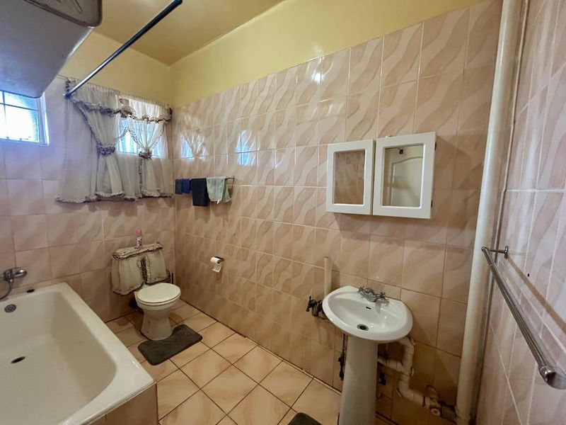 A dated bathroom featuring a pedestal sink, bathtub, and toilet with wall-to-wall tiling and exposed plumbing fixtures.