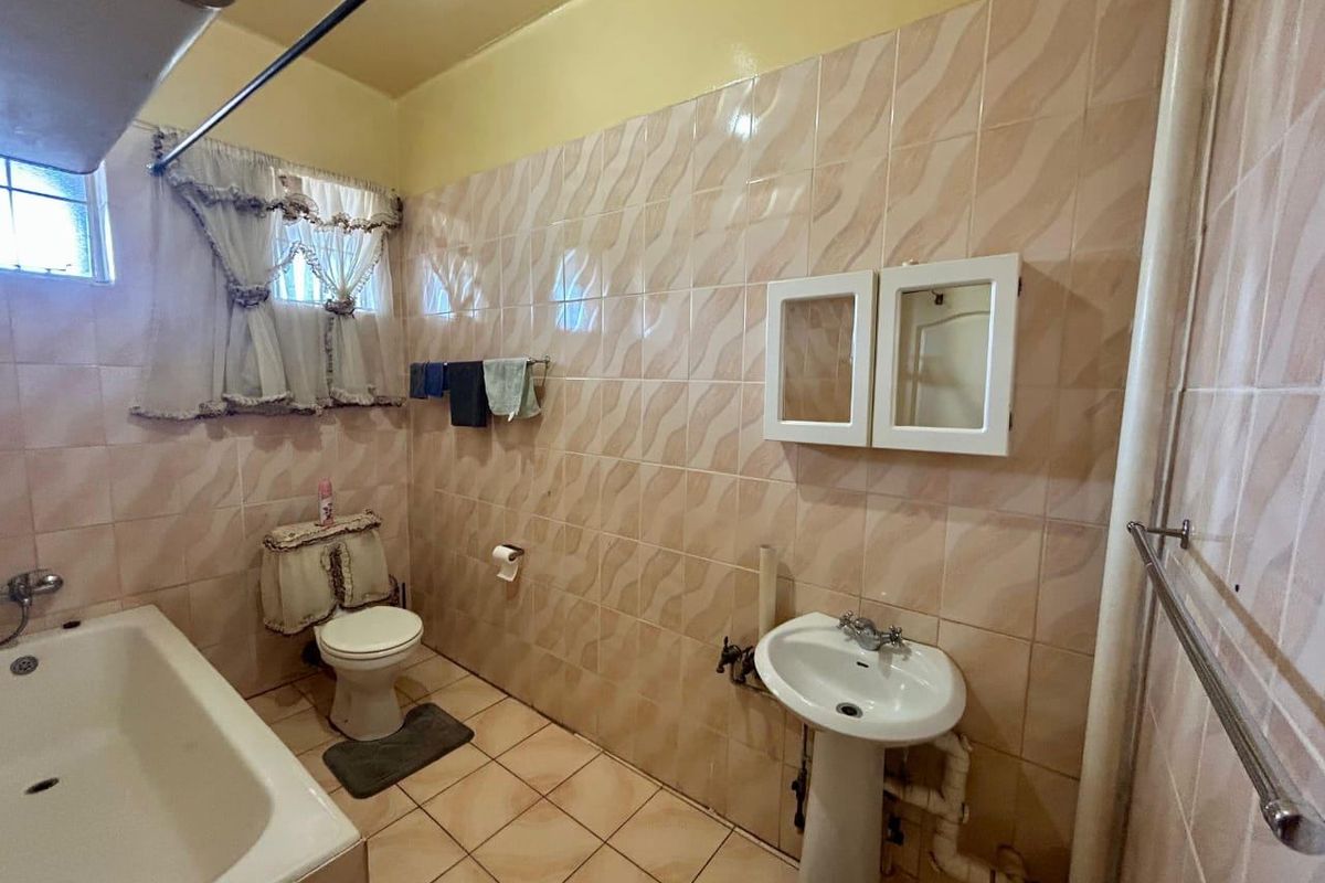 A dated bathroom featuring a pedestal sink, bathtub, and toilet with wall-to-wall tiling and exposed plumbing fixtures.