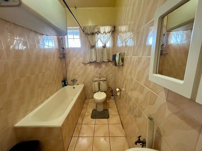 A dated bathroom featuring full-height wall tiling, a standard bathtub, and a toilet, offering potential for a modern renovation.