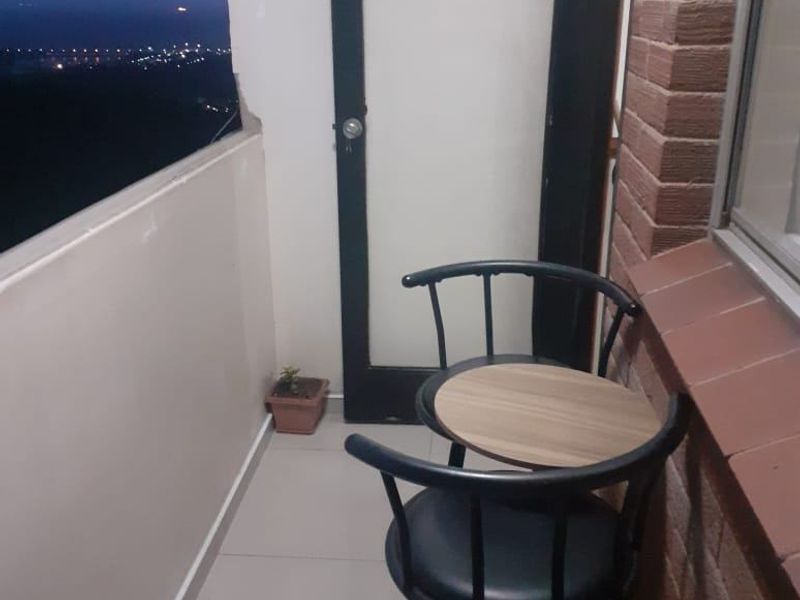 A compact balcony featuring tiled flooring, a brick exterior wall, and a glass-paneled door, offering an elevated view of the city lights at night.