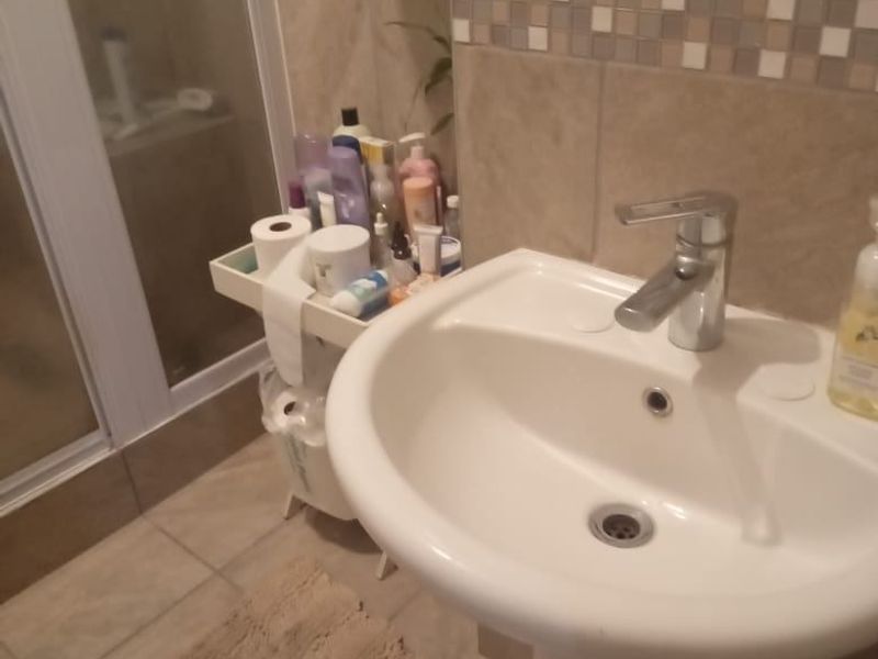 A functional bathroom featuring a pedestal basin with a chrome mixer tap and a separate shower enclosure with tiled finishes.