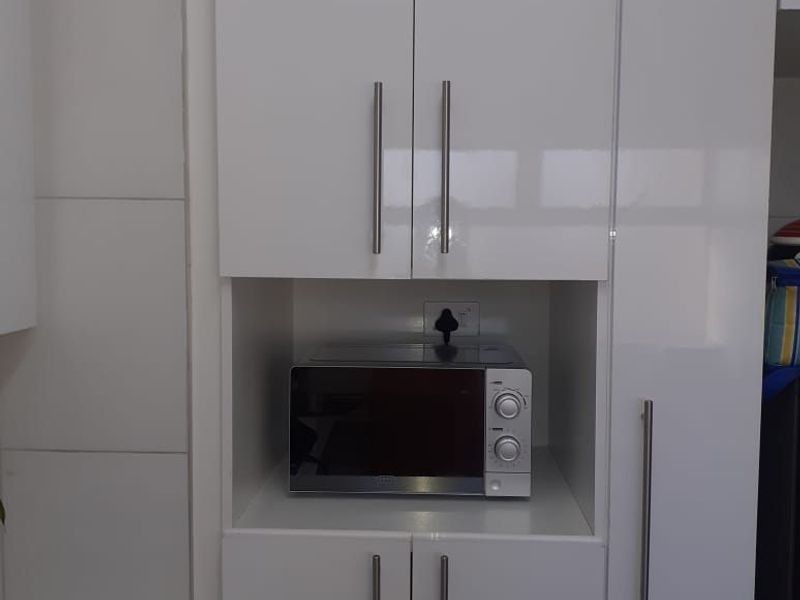 Modern kitchen featuring high-gloss white cabinetry, a dedicated microwave recess, and clean tiled splashbacks, offering a sleek and functional storage solution.