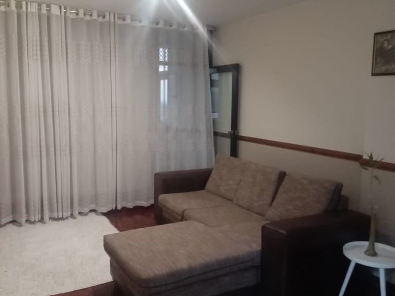 A living room featuring classic parquet flooring and a wooden dado rail, with large windows covered by floor-to-ceiling curtains.