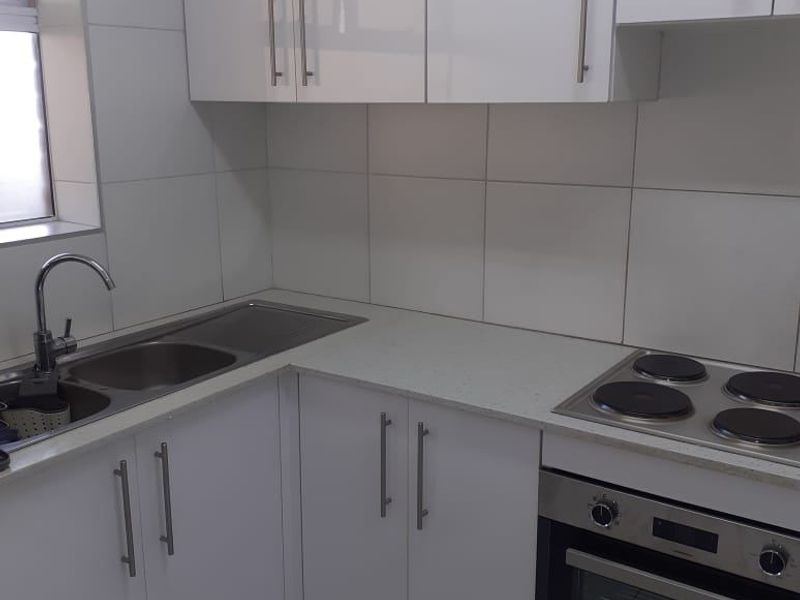A clean, modern kitchen featuring white gloss cabinetry, stainless steel appliances, a double sink, and neutral tiled finishes throughout.