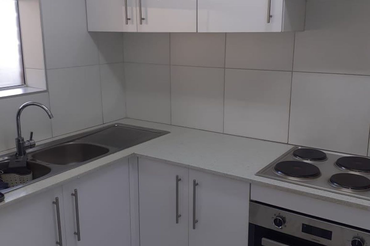 A clean, modern kitchen featuring white gloss cabinetry, stainless steel appliances, a double sink, and neutral tiled finishes throughout.