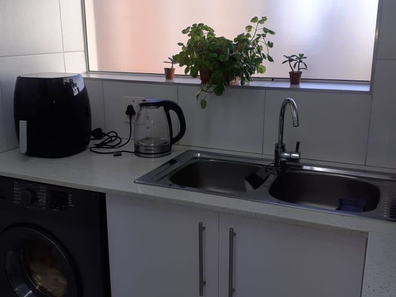 A functional laundry area featuring a stainless steel double sink, white cabinetry, stone countertops, and a tiled splashback under a large awning window.