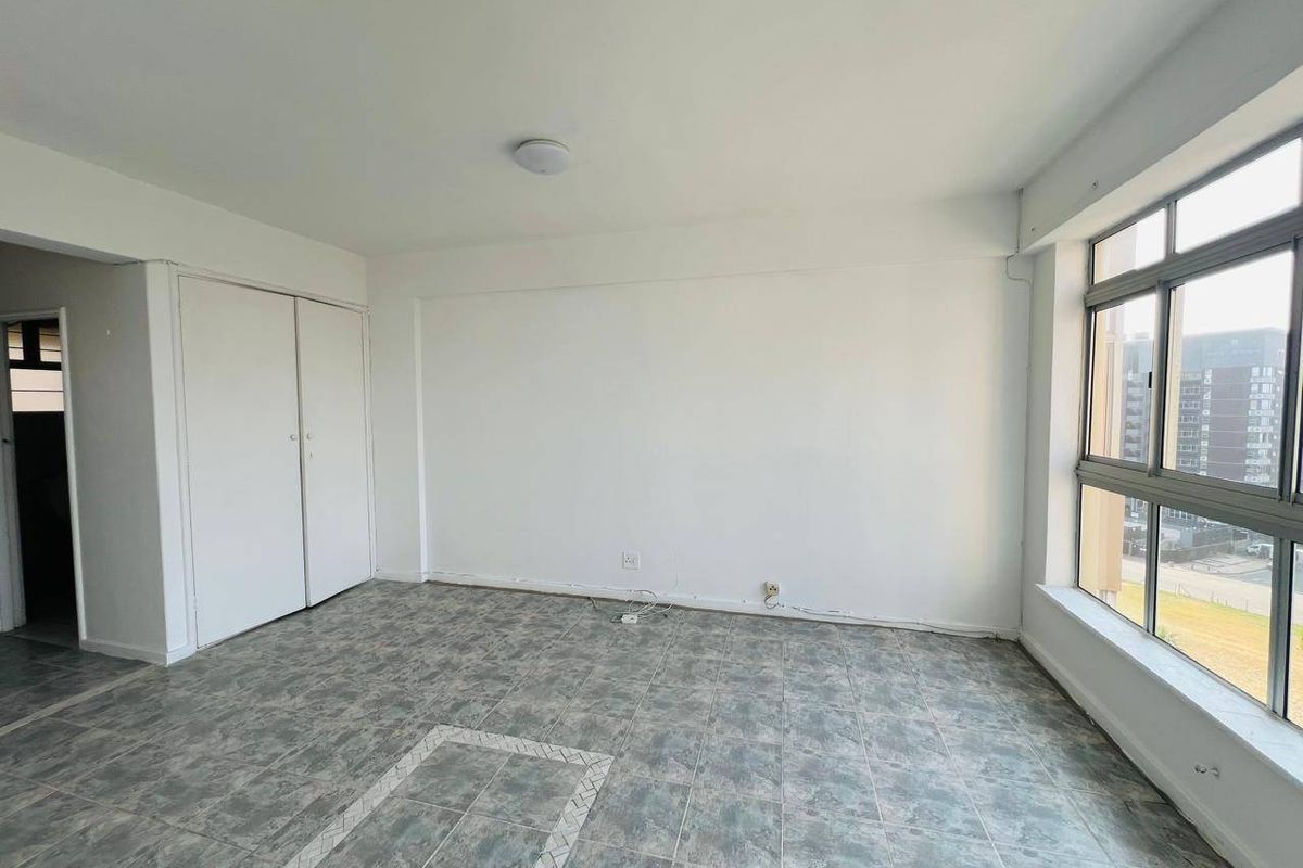 An empty bedroom featuring tiled flooring, built-in wardrobe storage, and large aluminium-framed windows providing natural light.