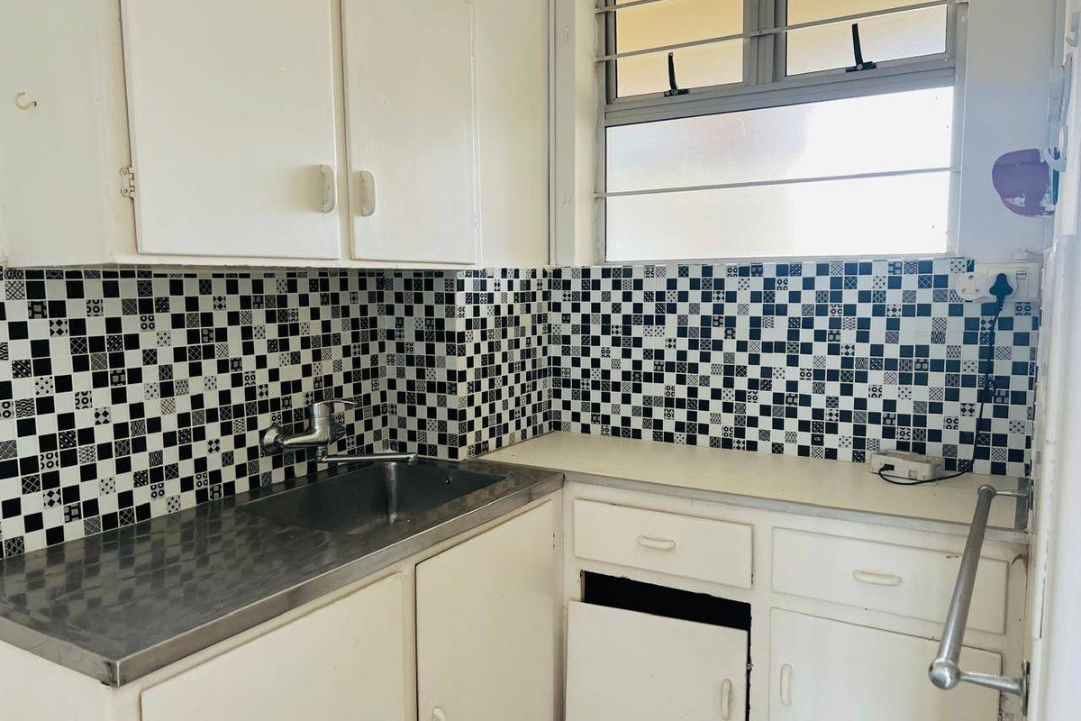A dated kitchen featuring a stainless steel sink, tiled backsplash, and built-in cabinetry, requiring cosmetic updates to modernize the space.