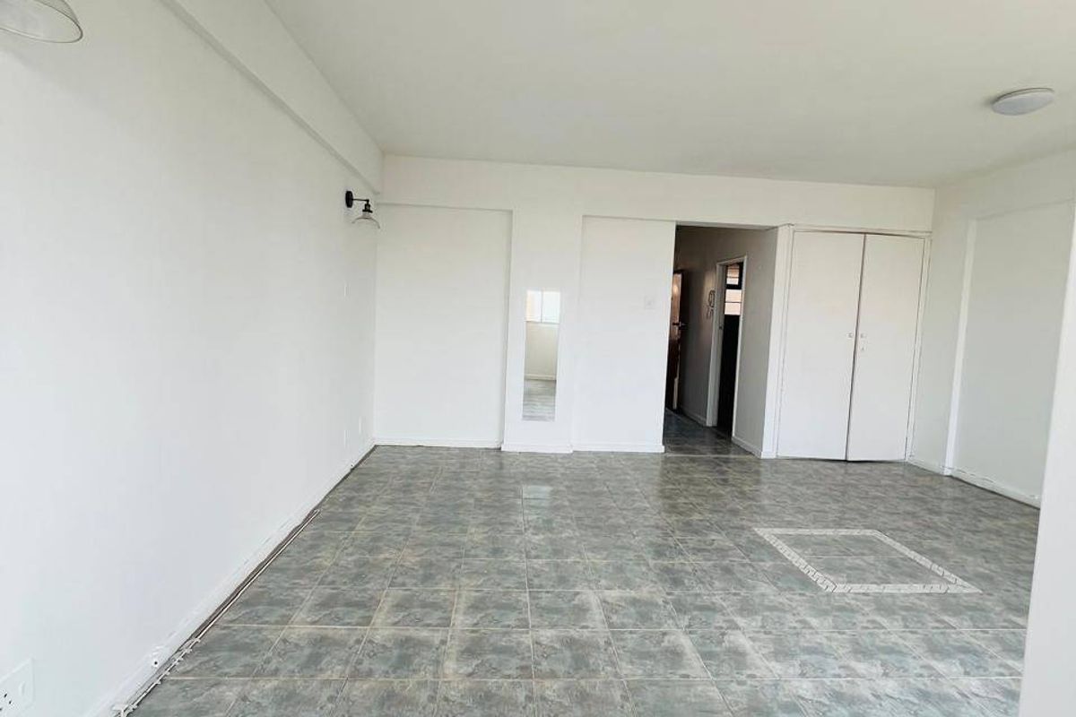 An empty, open-plan living area featuring tiled flooring, built-in storage cupboards, and wall-mounted lighting fixtures, ready for renovation or staging.