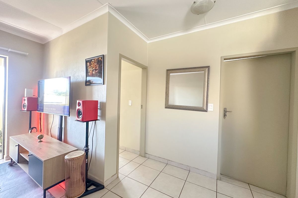 A living area featuring neutral wall tones, tiled flooring, and a functional layout with access to adjacent rooms.