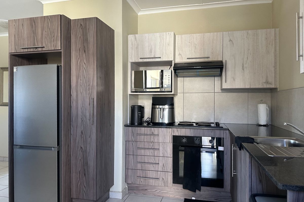 Modern kitchen featuring wood-grain cabinetry, granite countertops, built-in oven, hob, extractor fan, and integrated microwave with tiled flooring.