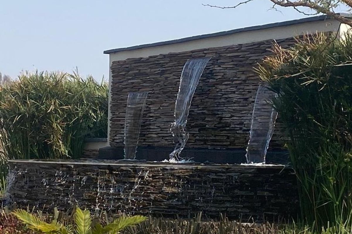 A decorative stone water feature with three cascading waterfalls set within a landscaped garden area.