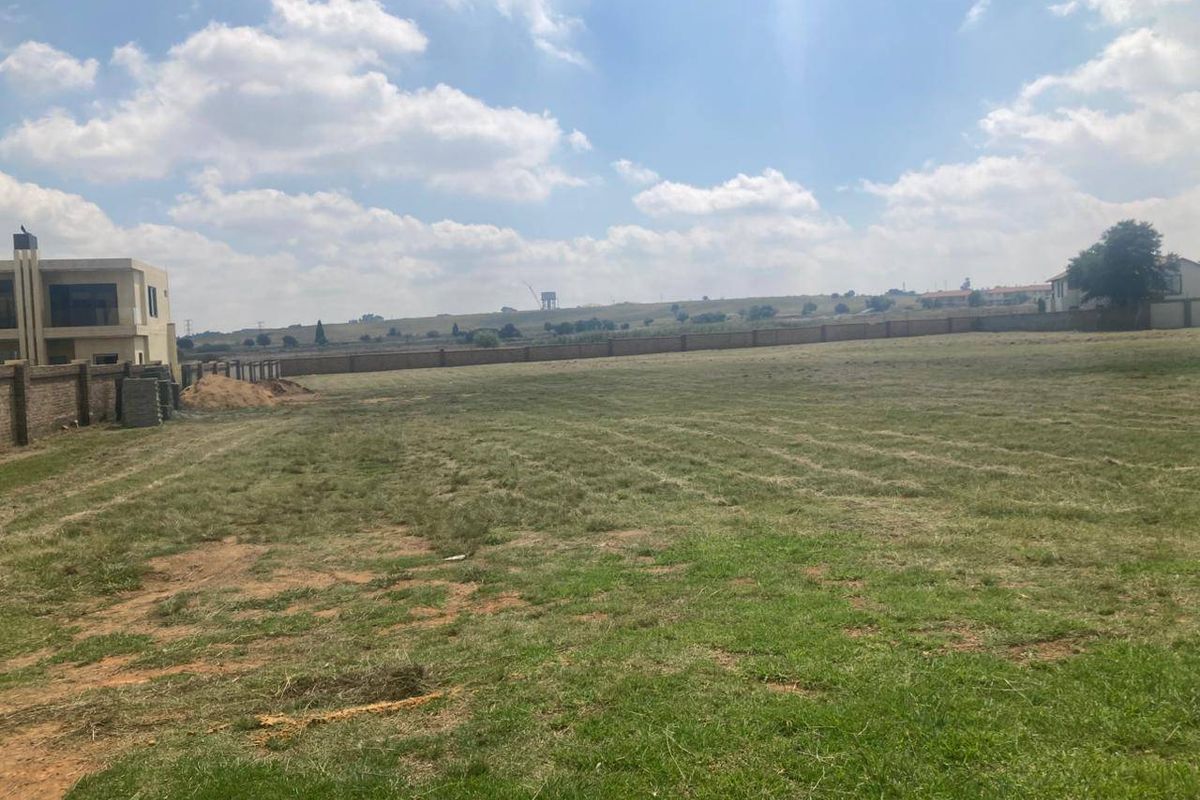 A spacious, level vacant residential plot featuring established grass cover and a perimeter boundary wall, offering a clear site for future development.