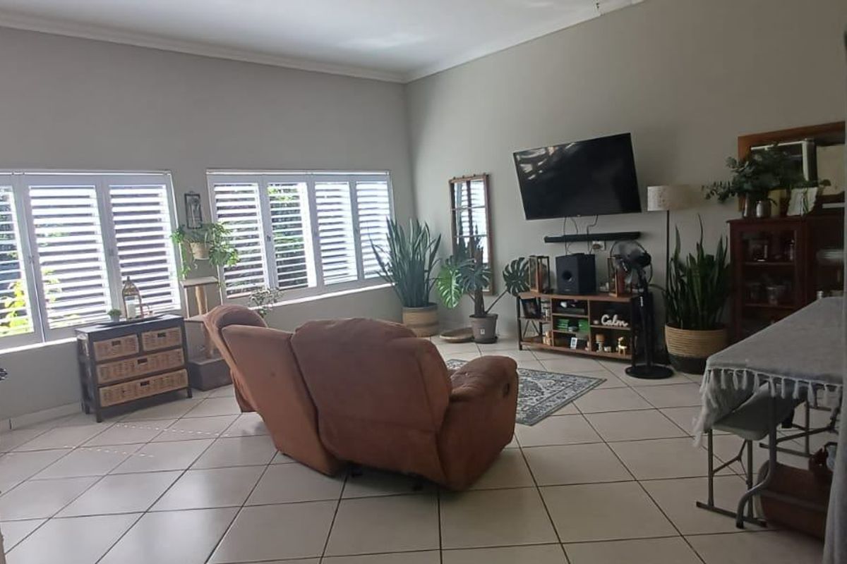 A spacious living room featuring neutral tiled flooring and white plantation shutters, offering a bright and functional living space.