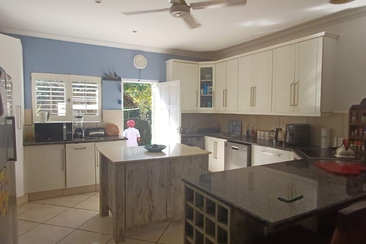 A functional kitchen featuring granite countertops, ample built-in cabinetry, a central island, and tiled flooring with direct access to the exterior.