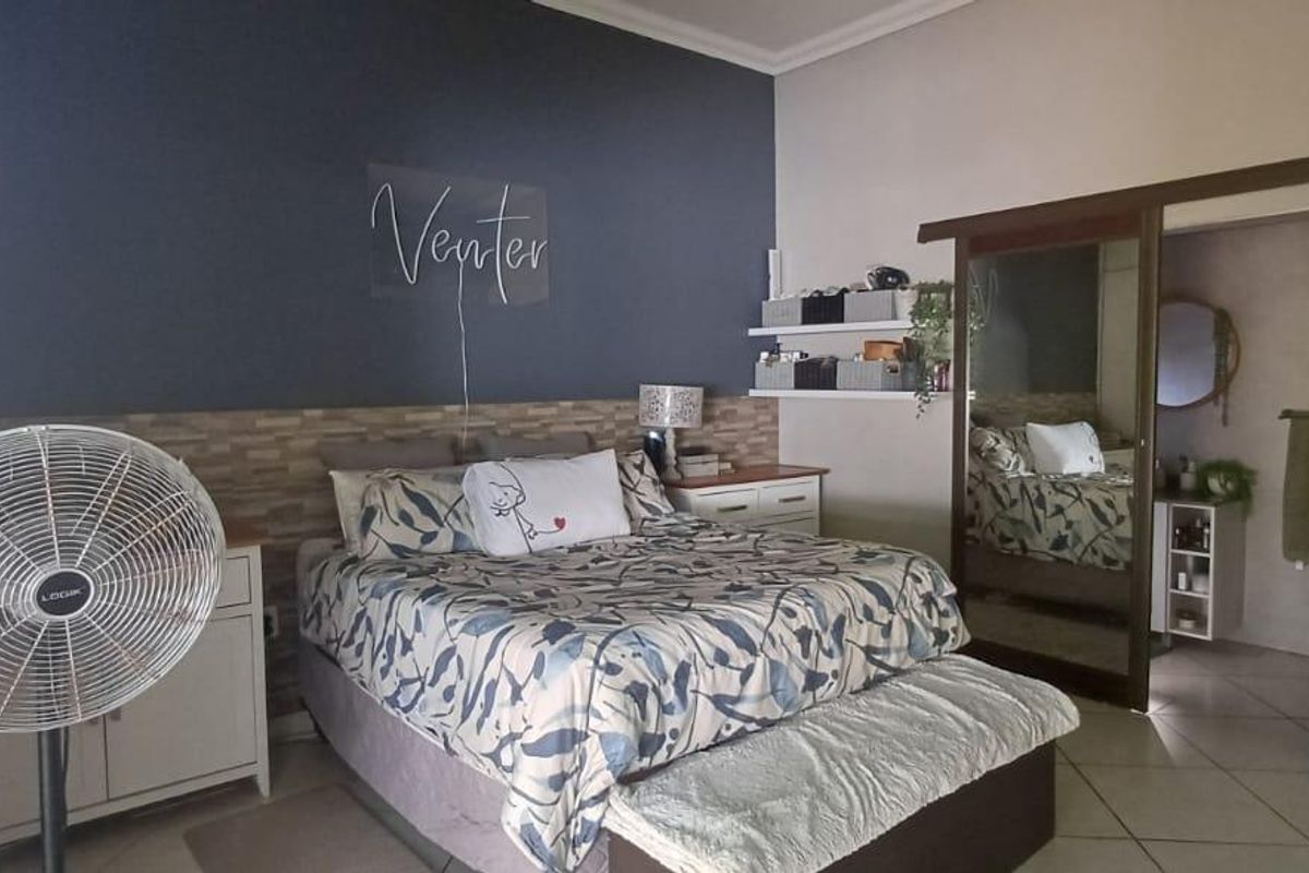 A well-maintained bedroom featuring tiled flooring, a dark accent wall, and a built-in sliding door wardrobe with mirror panels.