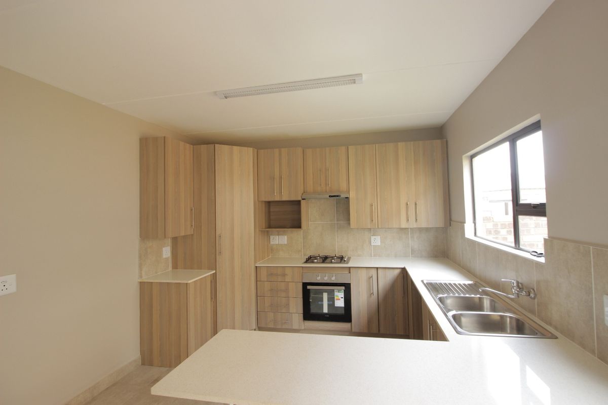 A clean, modern kitchen featuring light wood-finish cabinetry, stone countertops, a built-in oven, gas hob, and a double stainless steel sink.