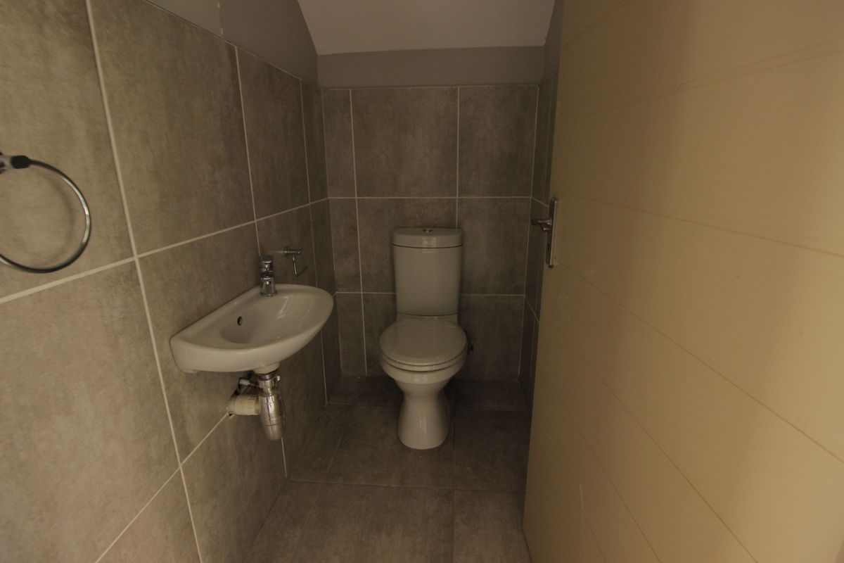 A compact guest bathroom featuring modern grey wall and floor tiles, a wall-mounted basin, and a standard toilet.