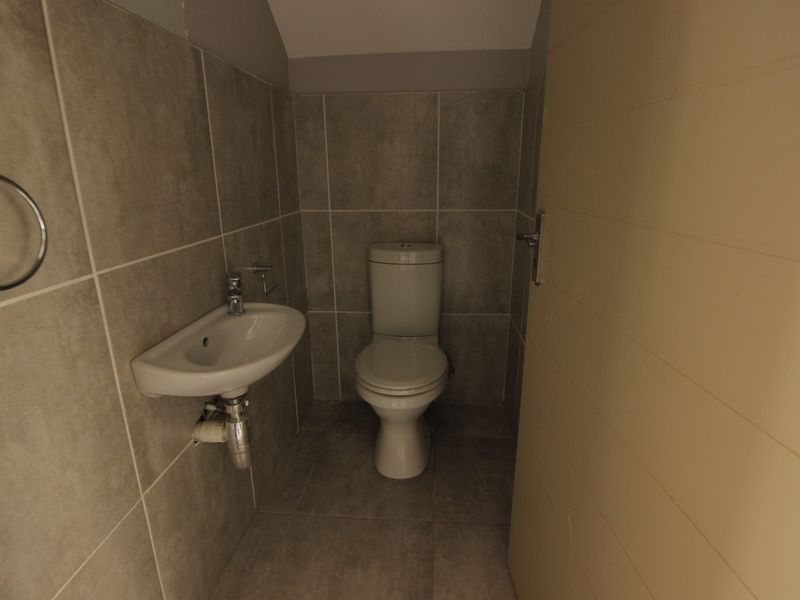 A compact guest bathroom featuring modern grey wall and floor tiles, a wall-mounted basin, and a standard toilet.