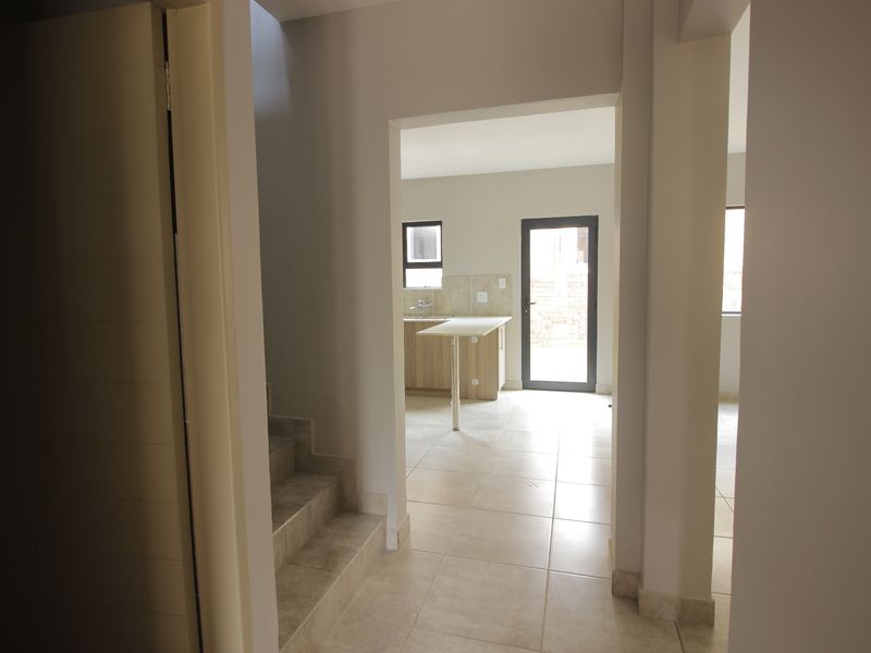 A view from the hallway looking into an open-plan kitchen area with tiled flooring and neutral finishes.