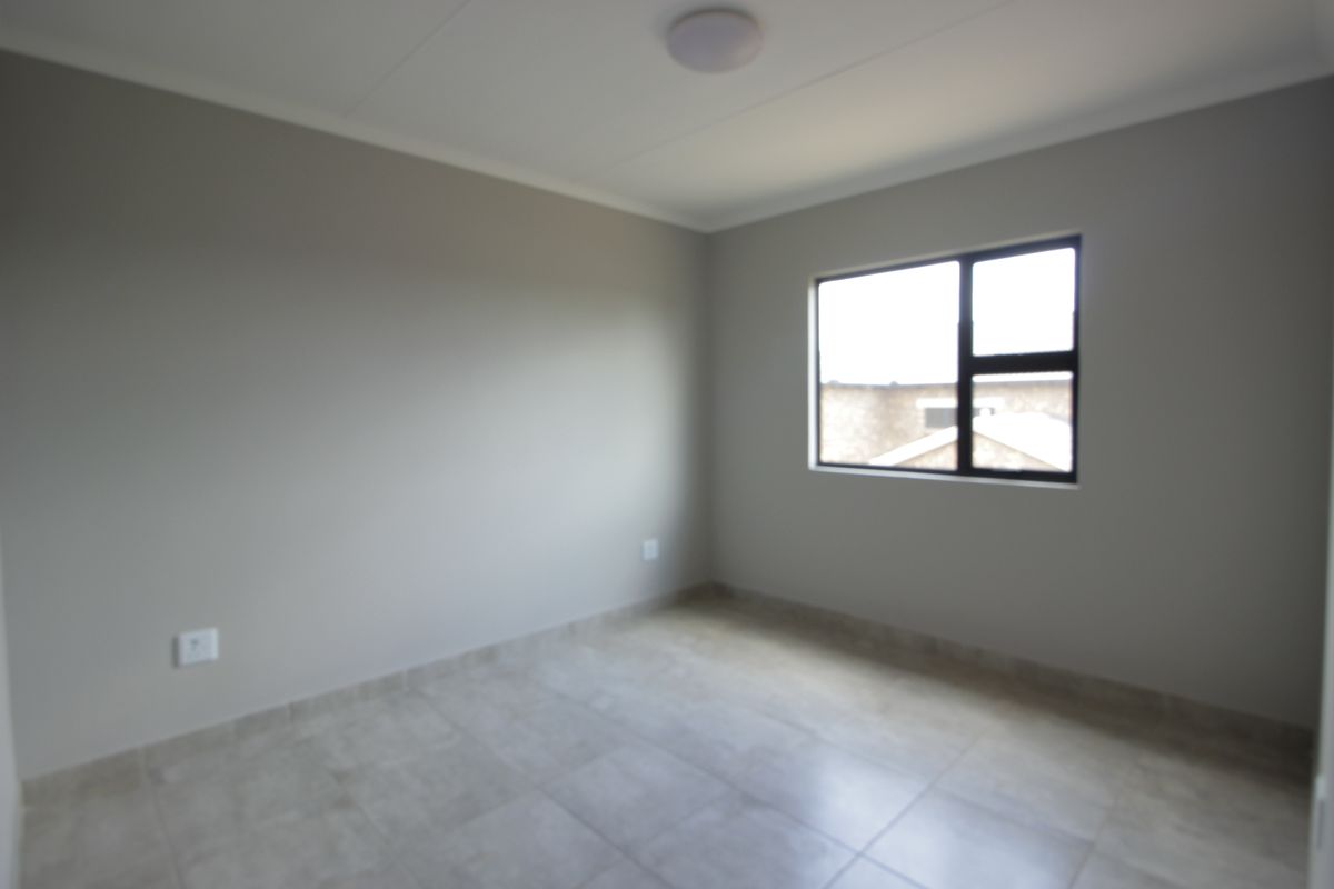 A clean, empty bedroom featuring neutral wall paint, tiled flooring, and an aluminium-framed window, providing a blank canvas for interior design.